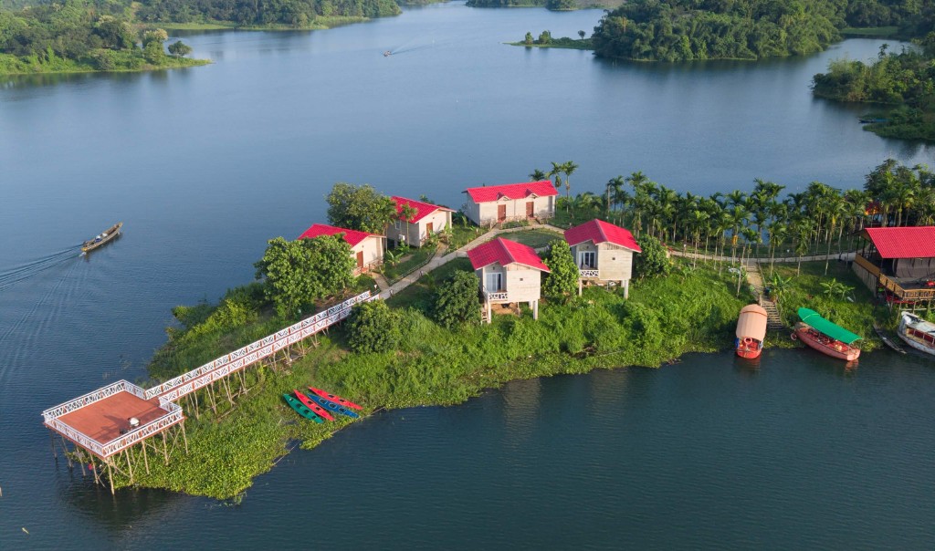 Aerial view of Furomon Island Resort — red-roof cottages, white pier, and kayaks on Kaptai Lake